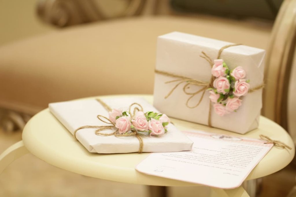 Beautifully wrapped wedding gifts with delicate pink floral decorations on a beige table, exemplifying modern wedding registry etiquette and personalized gift selections. Perfect representation for topics on wedding registry etiquette, wedding etiquette, and wedding registry tips for 2024.