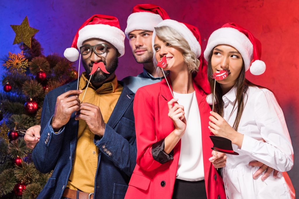 multicultural businesspeople holding lips and glasses on sticks at Christmas corporate party