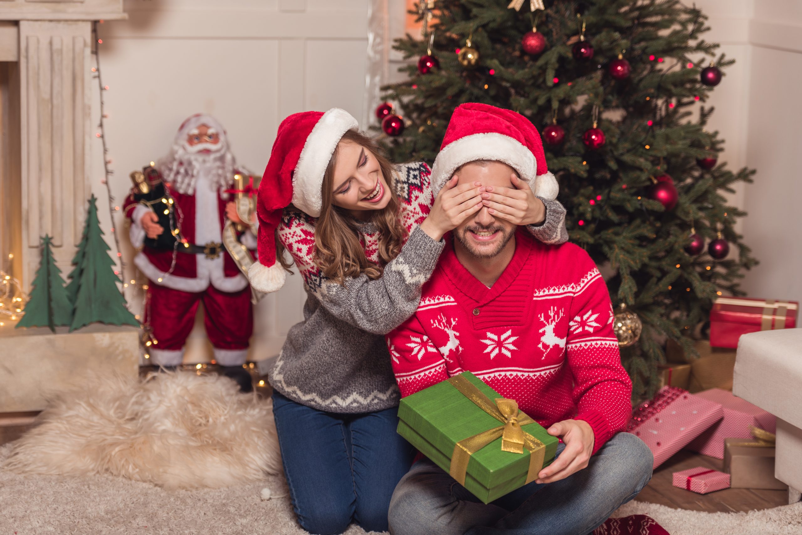 smiling young woman closing eyes to happy man with christmas present