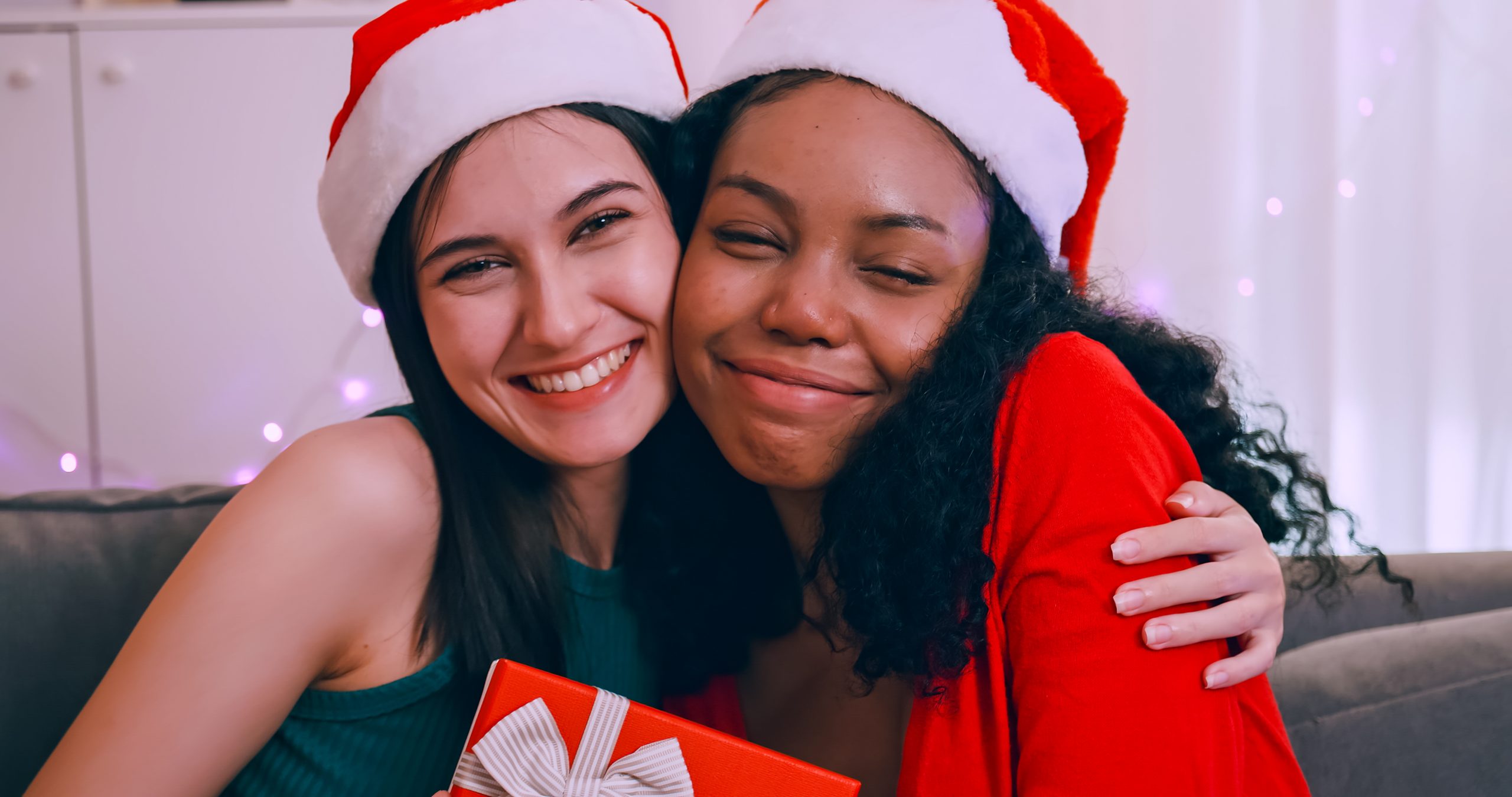 Young woman surprising her girlfriend with Christmas gift. Cheer