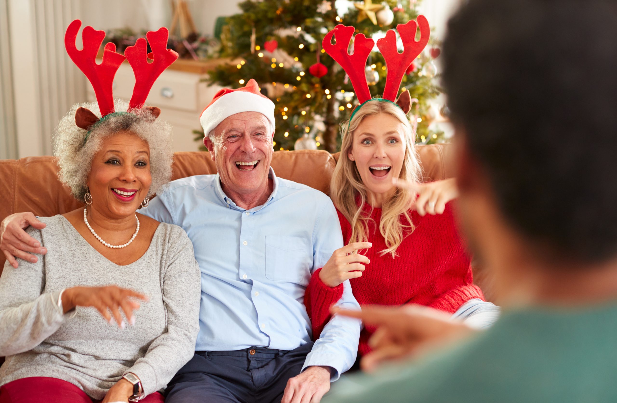 Adult Family Sitting On Sofa Playing Game Of Charades At Christmas Together