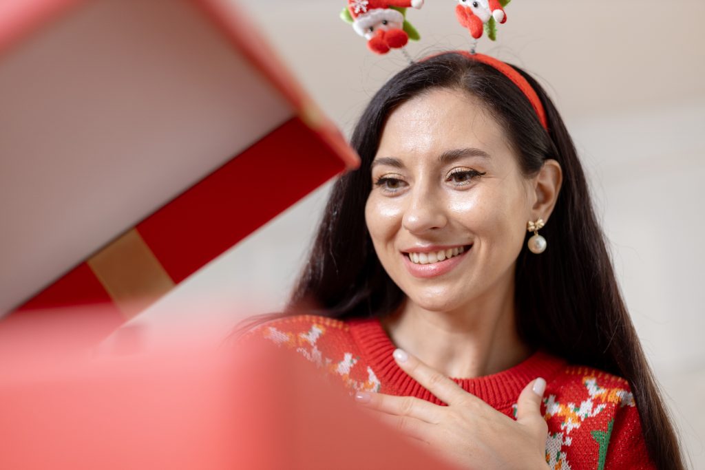 Christmas day concept. woman sitting surprised and opening gift box with christmas tree background. Festive atmosphere party.