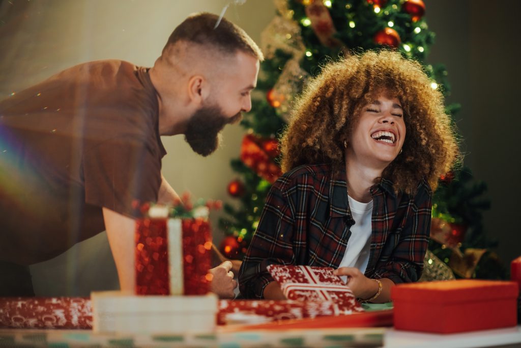 Couple happily wraps christmas presents together at a cozy table. Surrounded by festive decorations and twinkling lights. Sharing laughter and love as they prepare surprises for family and friends