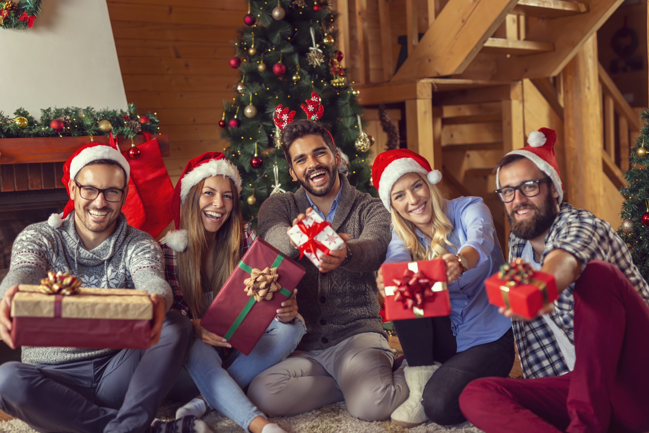 Group of friends sitting next to a fireplace and a nicely decorated Christmas tree, having fun on Christmas morning, exchanging Christmas presents