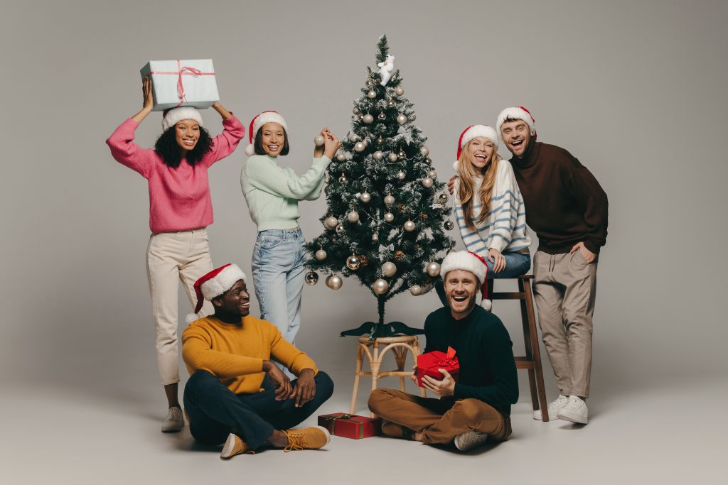 Group of young people smiling while having fun near the Christmas tree on studio background together