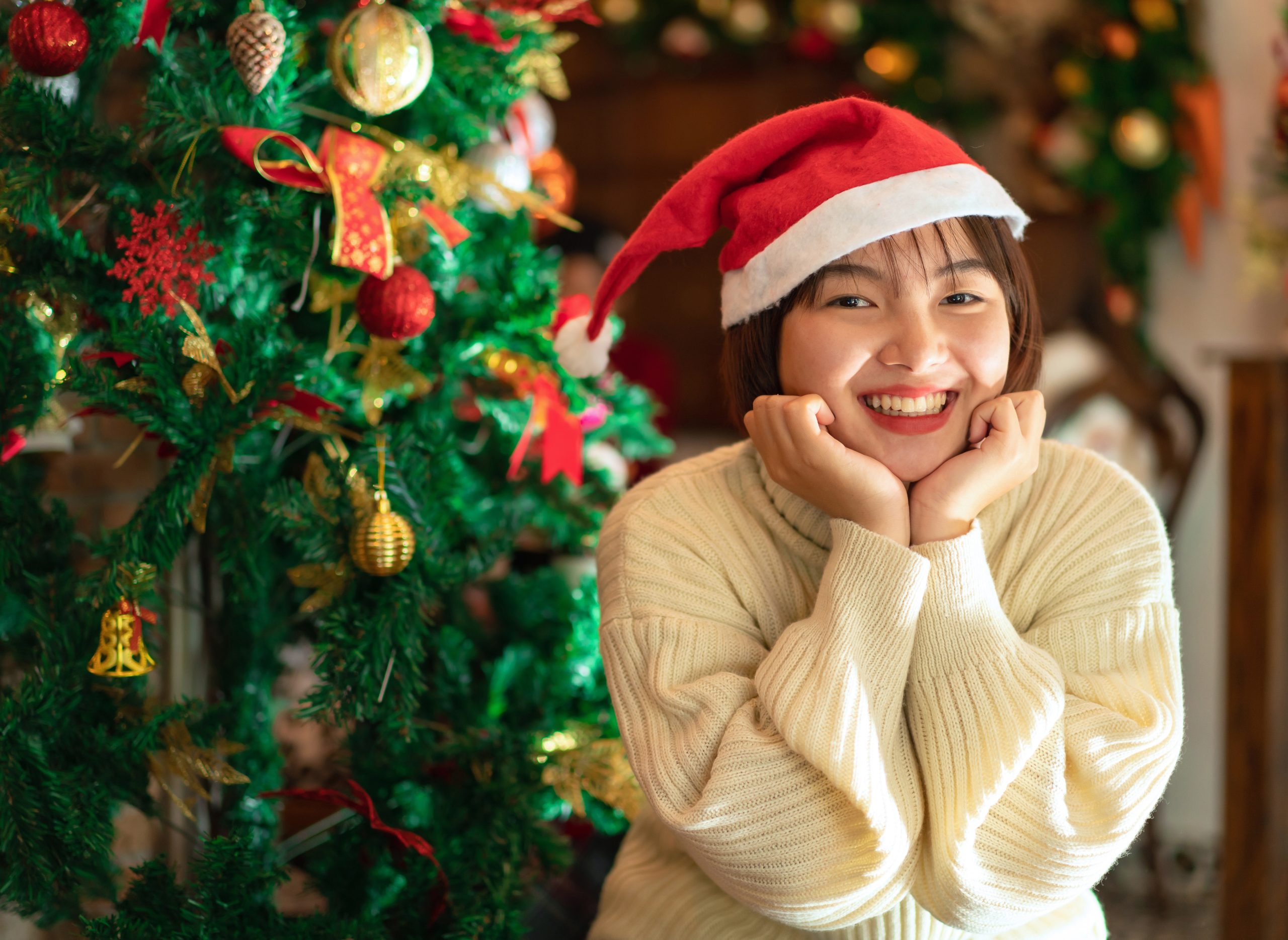 Happy beautiful woman in santa hat is smiling and looking at the camera to posing take a photo while sitting in living room at home with christmas interior