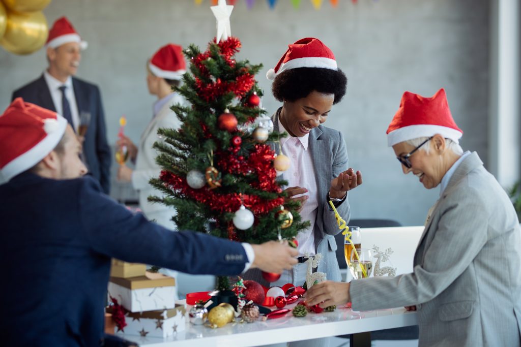 Happy African American businesswoman and her coworkers having fun while decorating Christmas tree in the office.