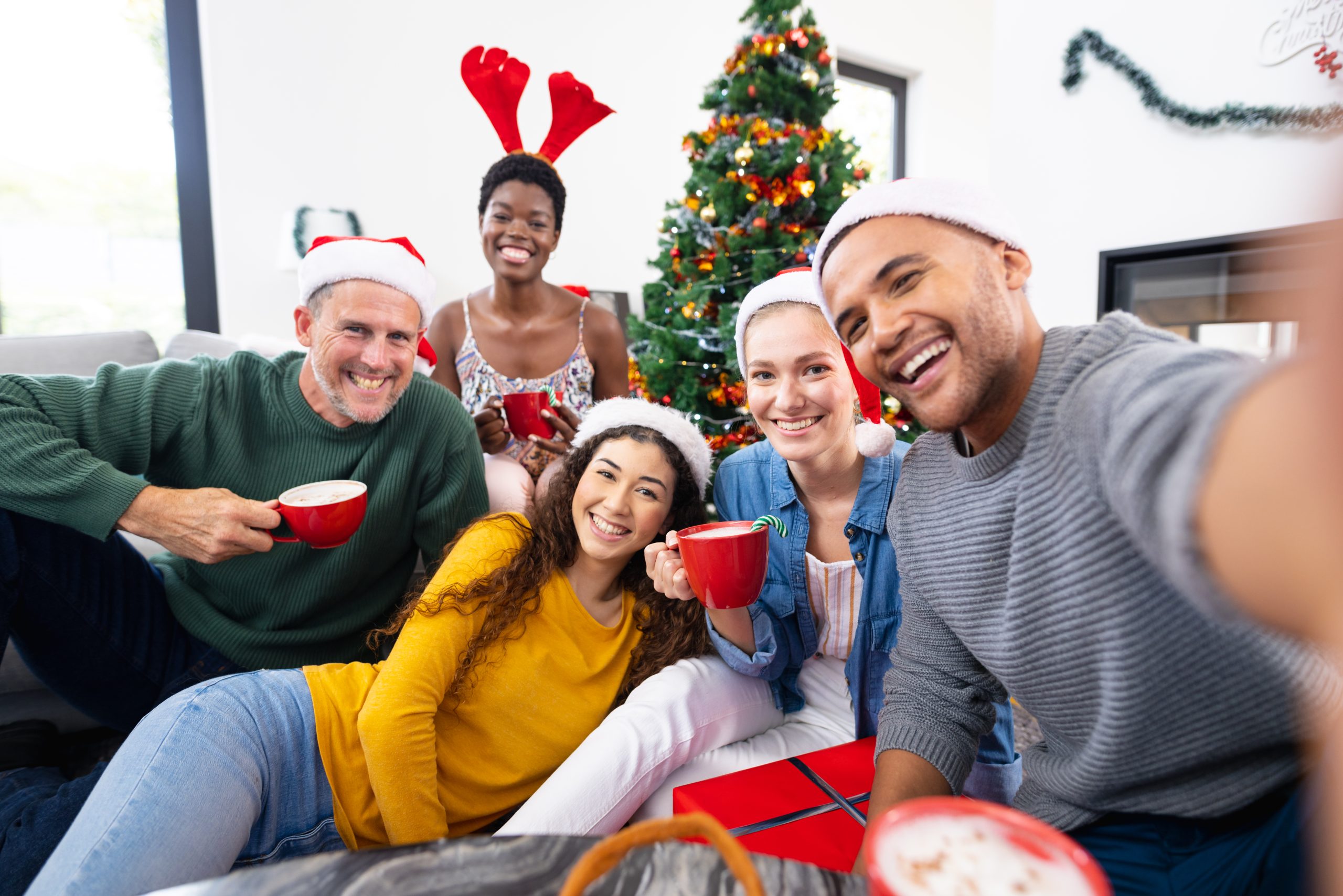 Image of happy diverse friends celebrating christmas at home taking selfie. Christmas, celebration, tradition, friendship, inclusivity and lifestyle concept.