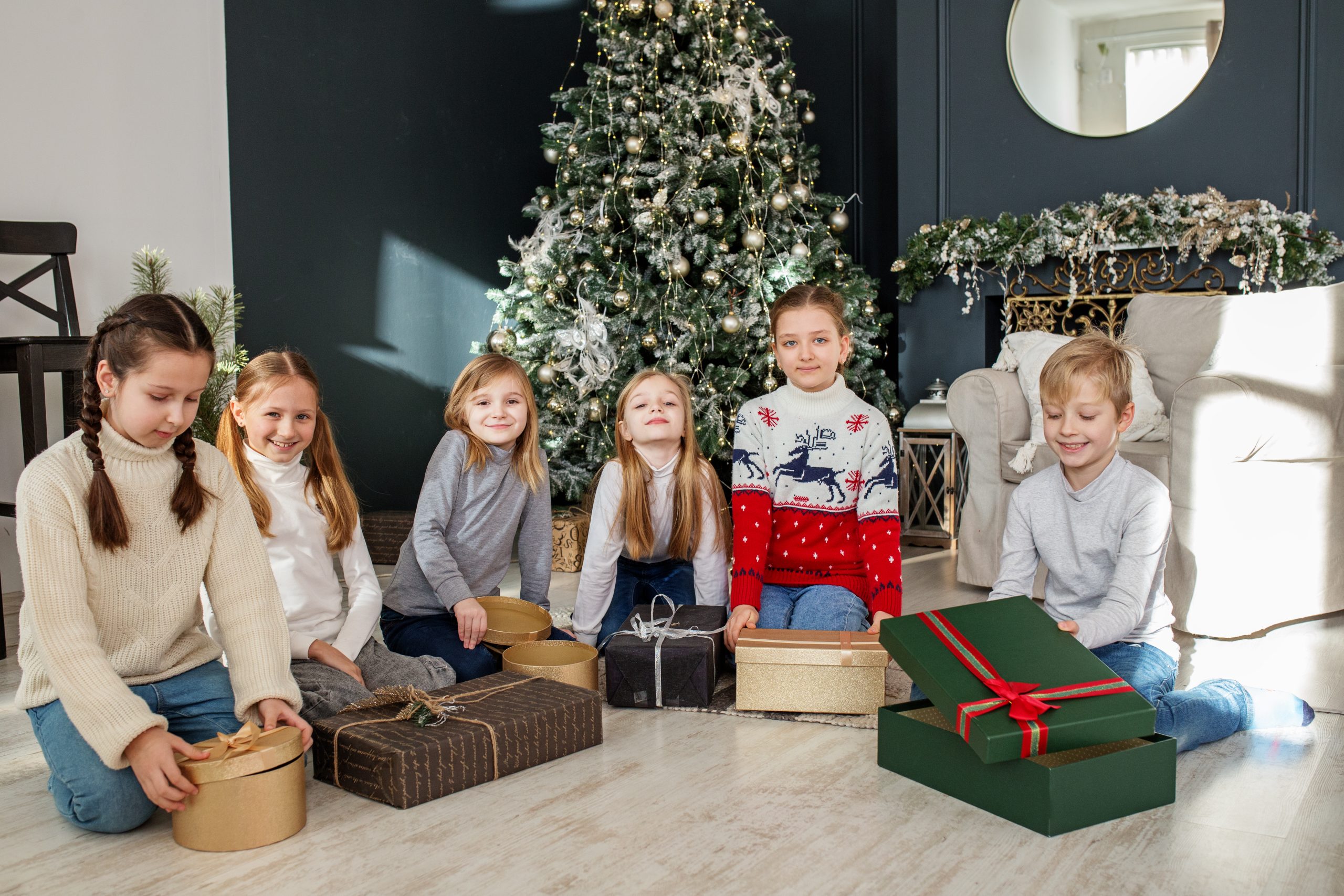 Merry Christmas and Happy Holidays. Group of smiling diverse children sitting on floor in cozy decorated living-room after exchanging Xmas presents at fun party at home