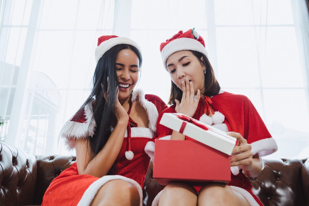 Two Santa women open gift boxes together.