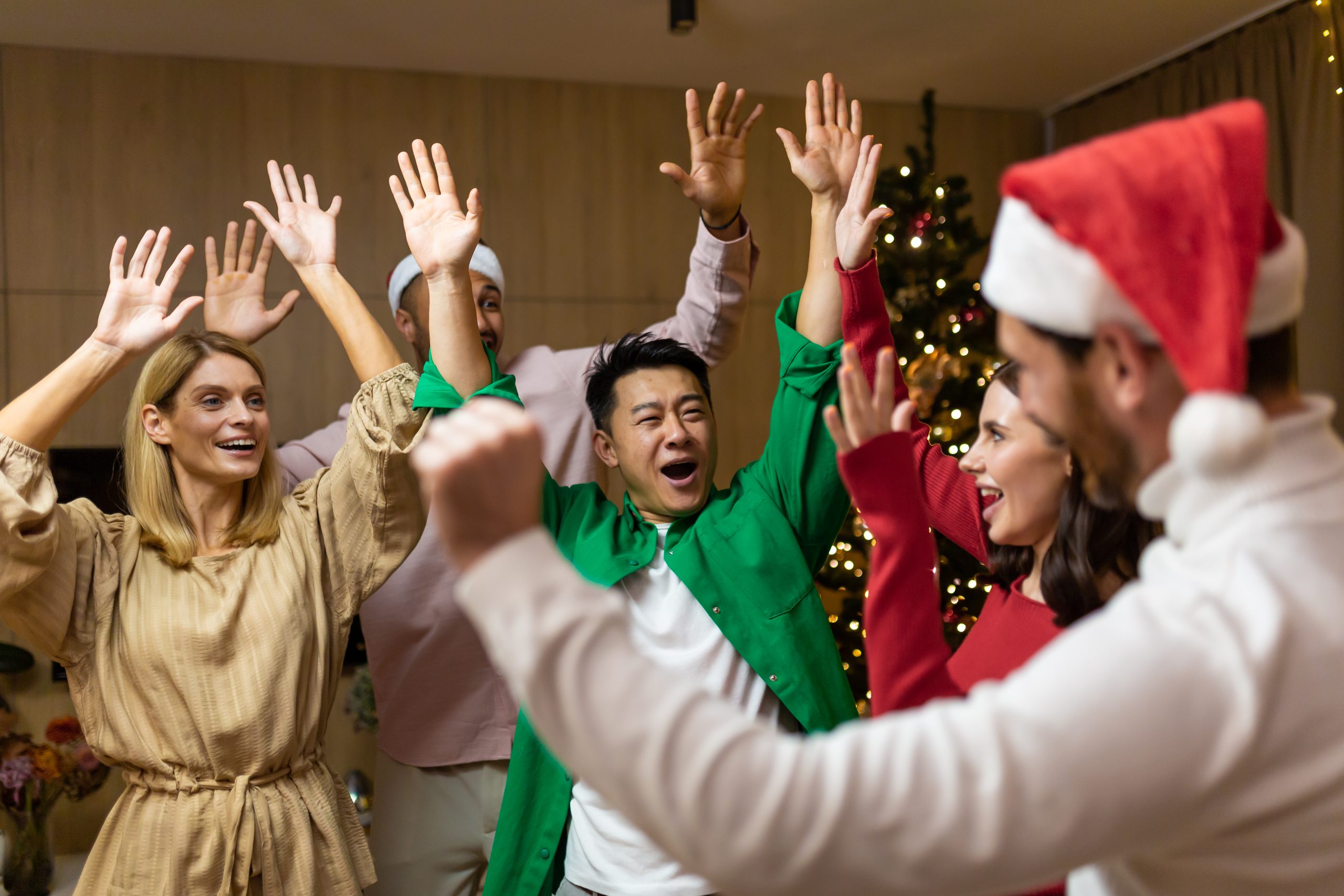 New Year holiday party. Young beautiful interracial people, men and women, dancing and having fun at home near the Christmas tree.