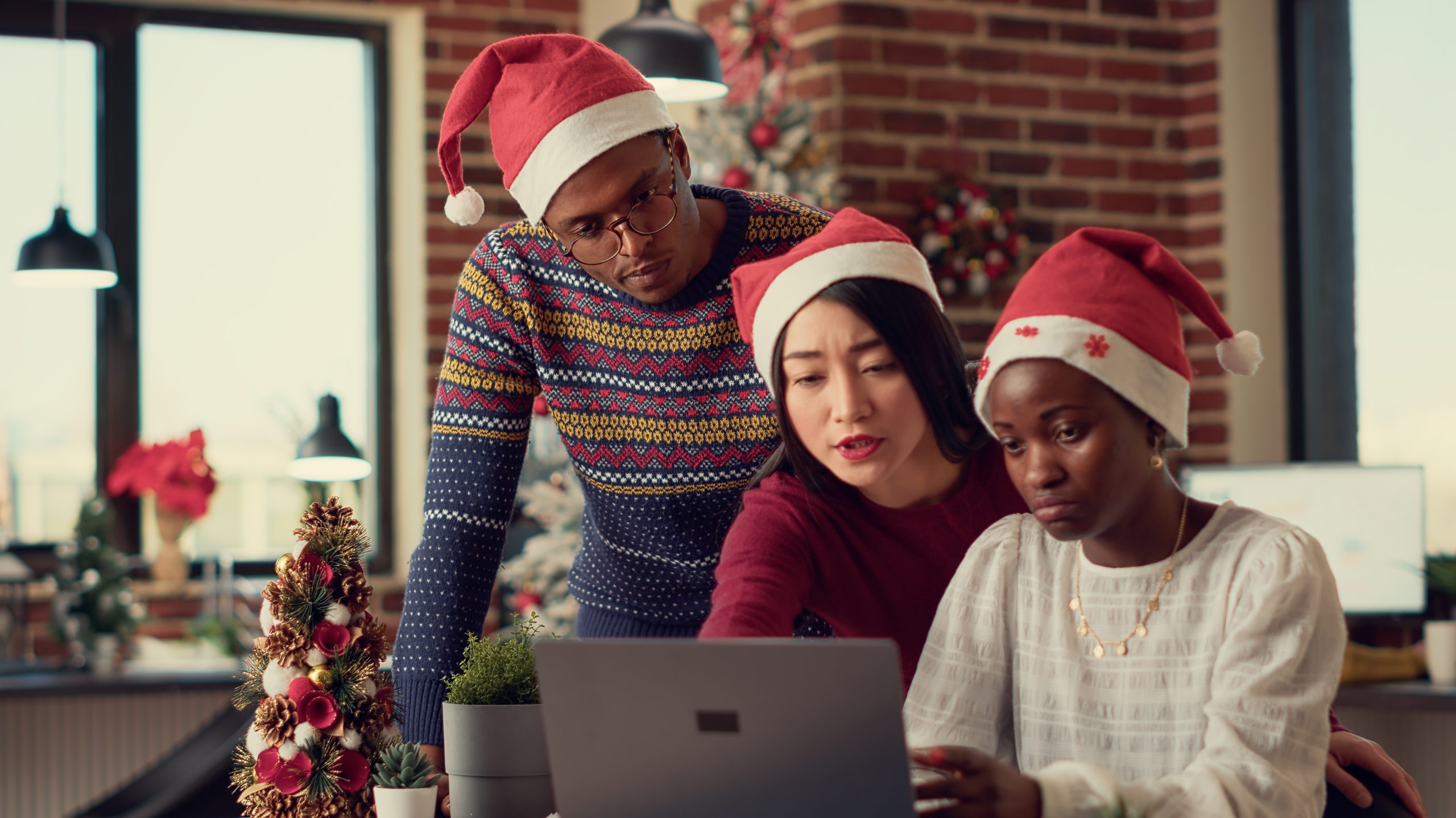 Diverse group of people working together on startup project in office with christmas tree and festive decorations. Colleagues at job before celebrating winter holiday season with xmas lights.