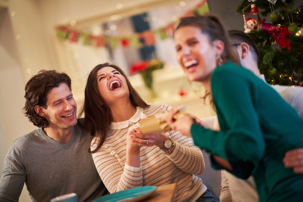 Picture showing group of friends pulling Christmas crackers at home