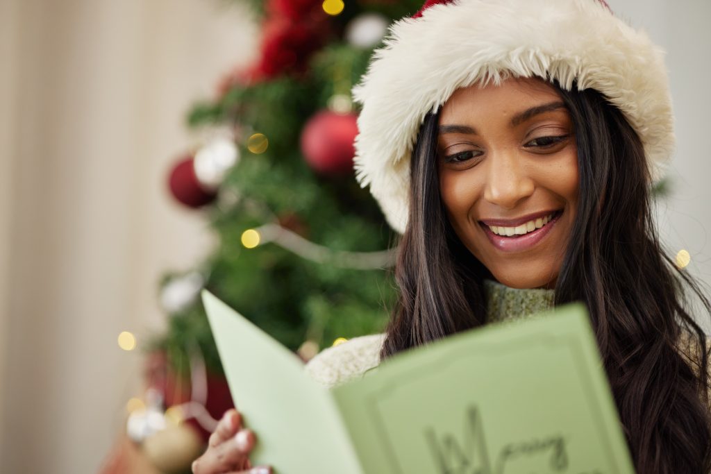 Happy woman reading Christmas card, note or message in home living room in winter holiday celebrati.