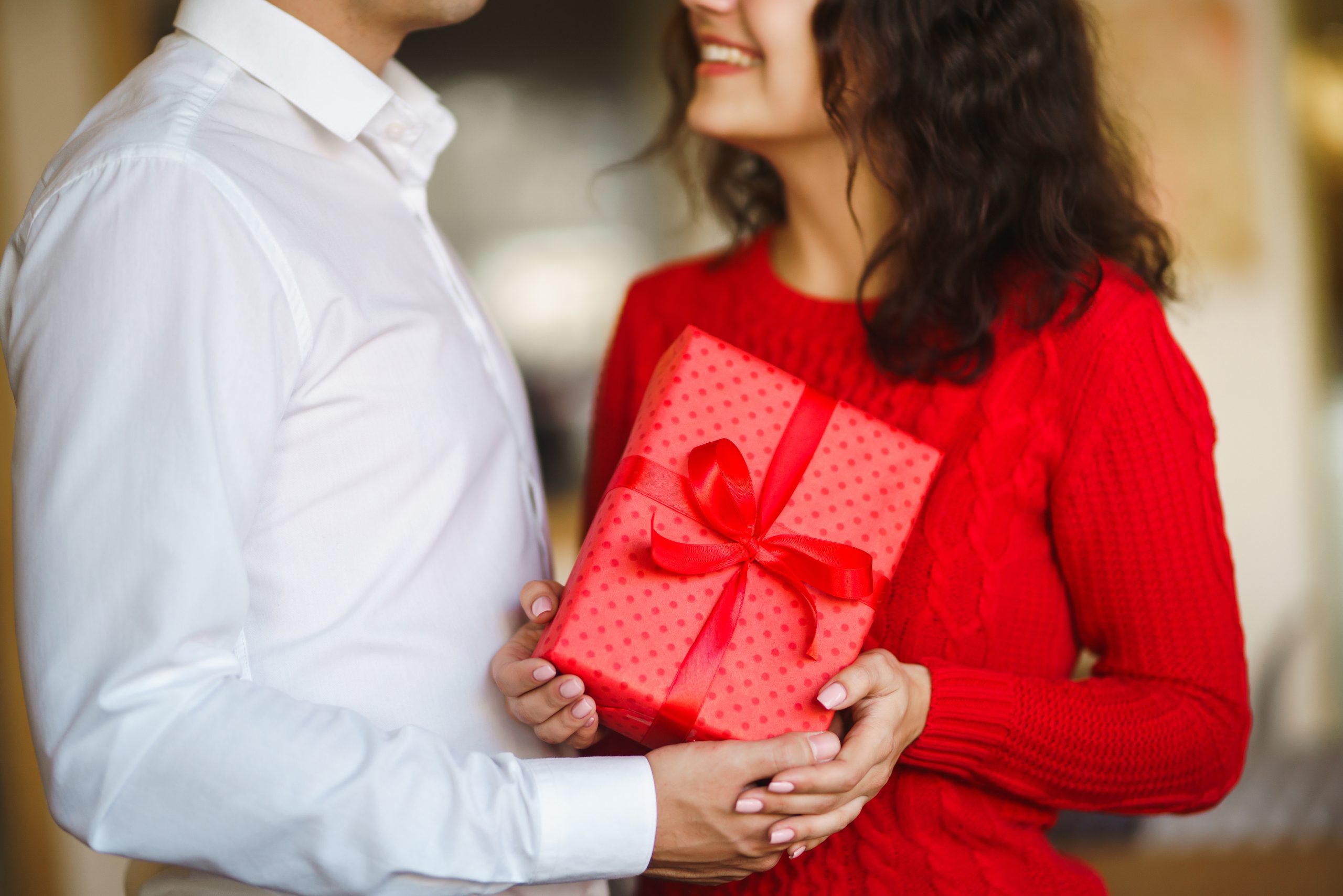 A young man gives his beloved a present and closes her eyes with a hand. Valentine's Day.