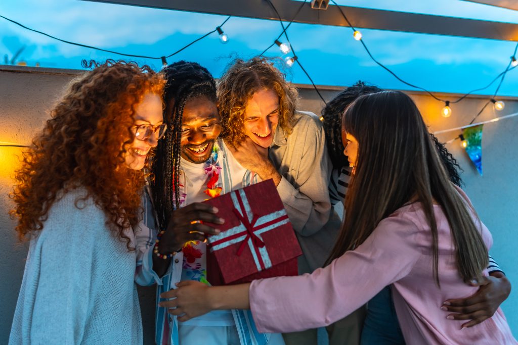 man opening birthday present embraced by his friends