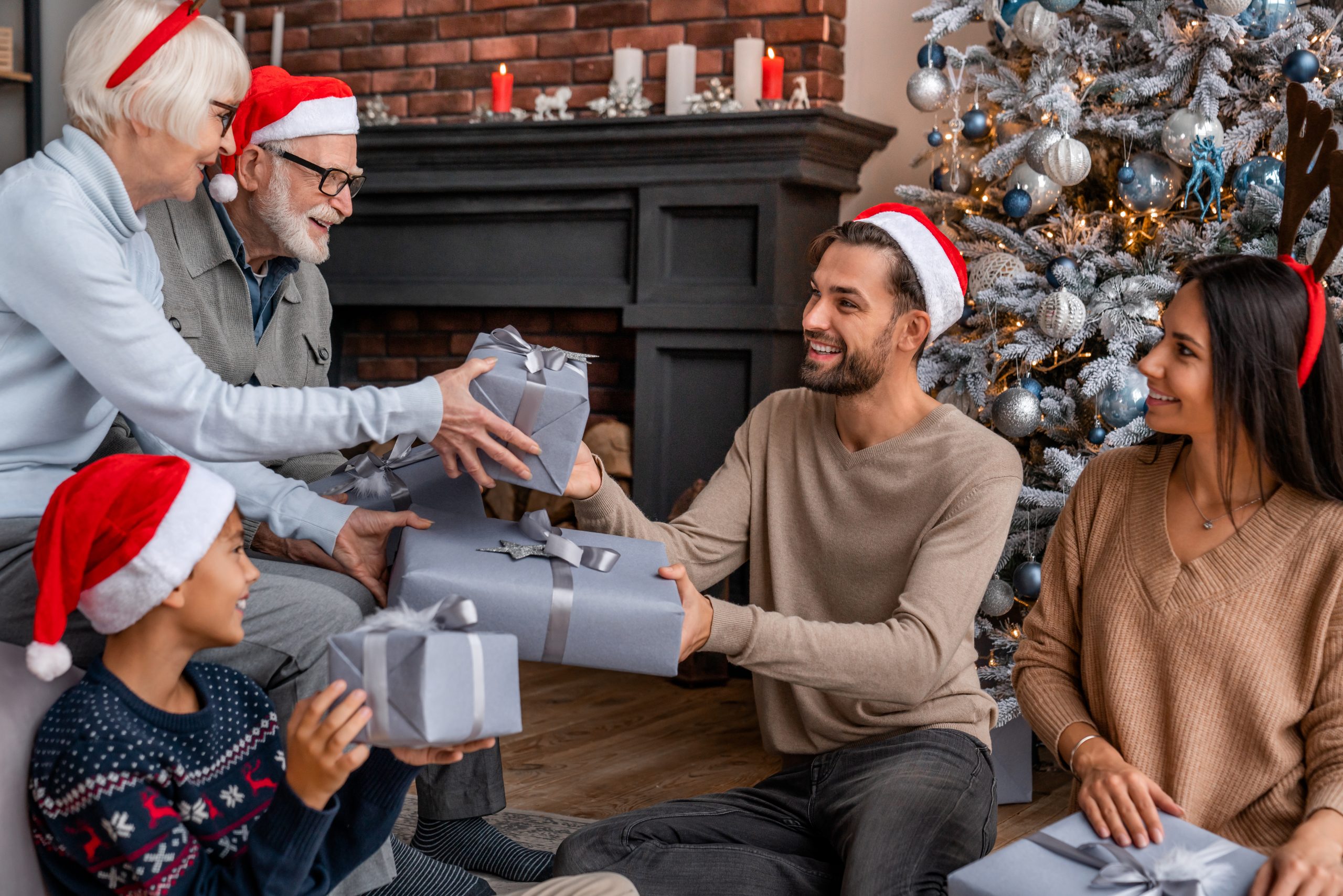 Happy family sitting near Christmas tree in living room exchanging christmas presents