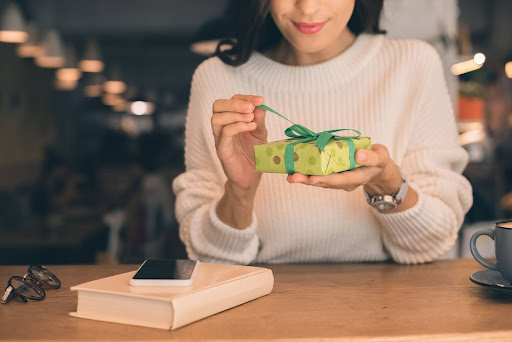 Woman opening gift over desk with book and phone next to her