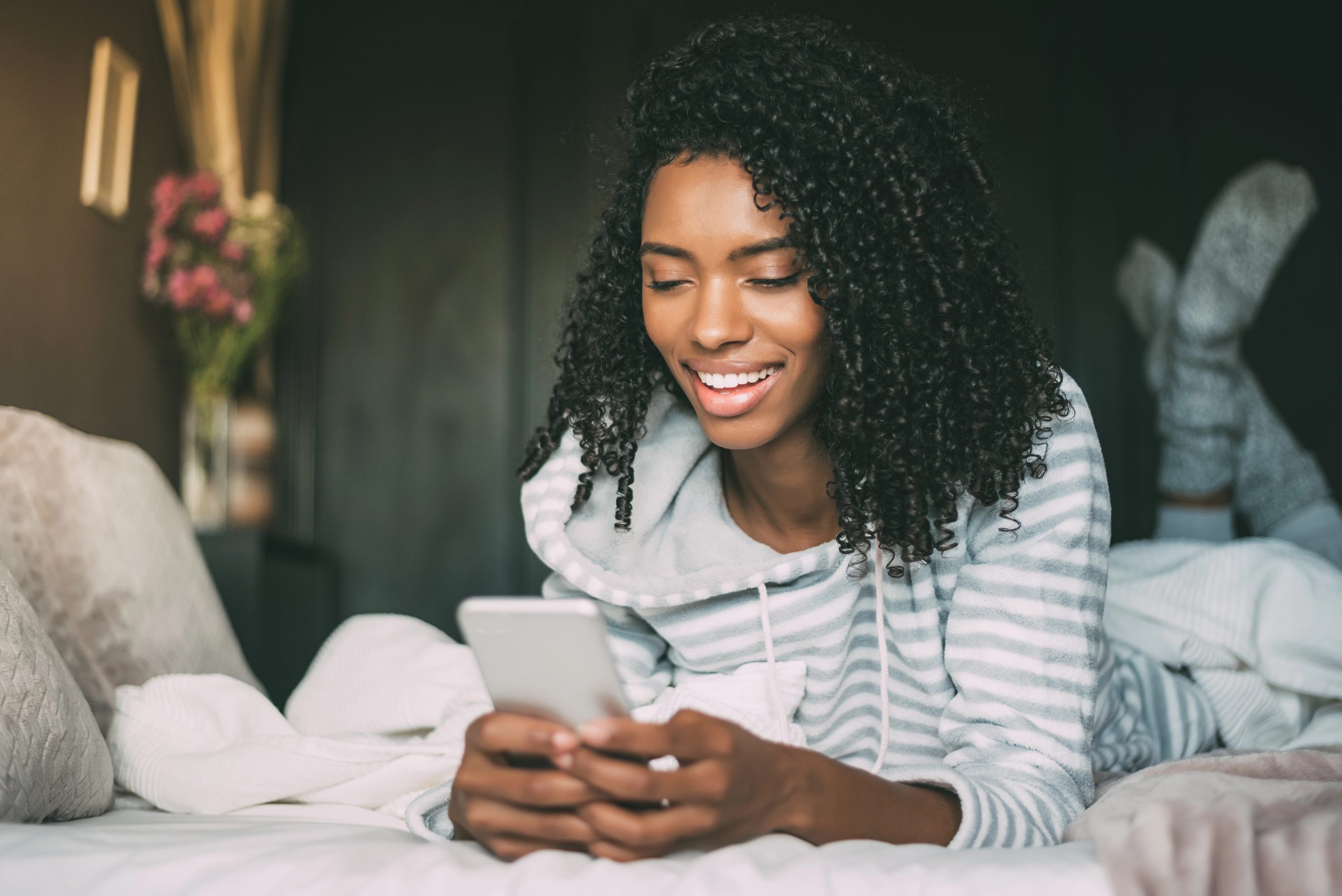 happy young woman laying on bed looking at phone