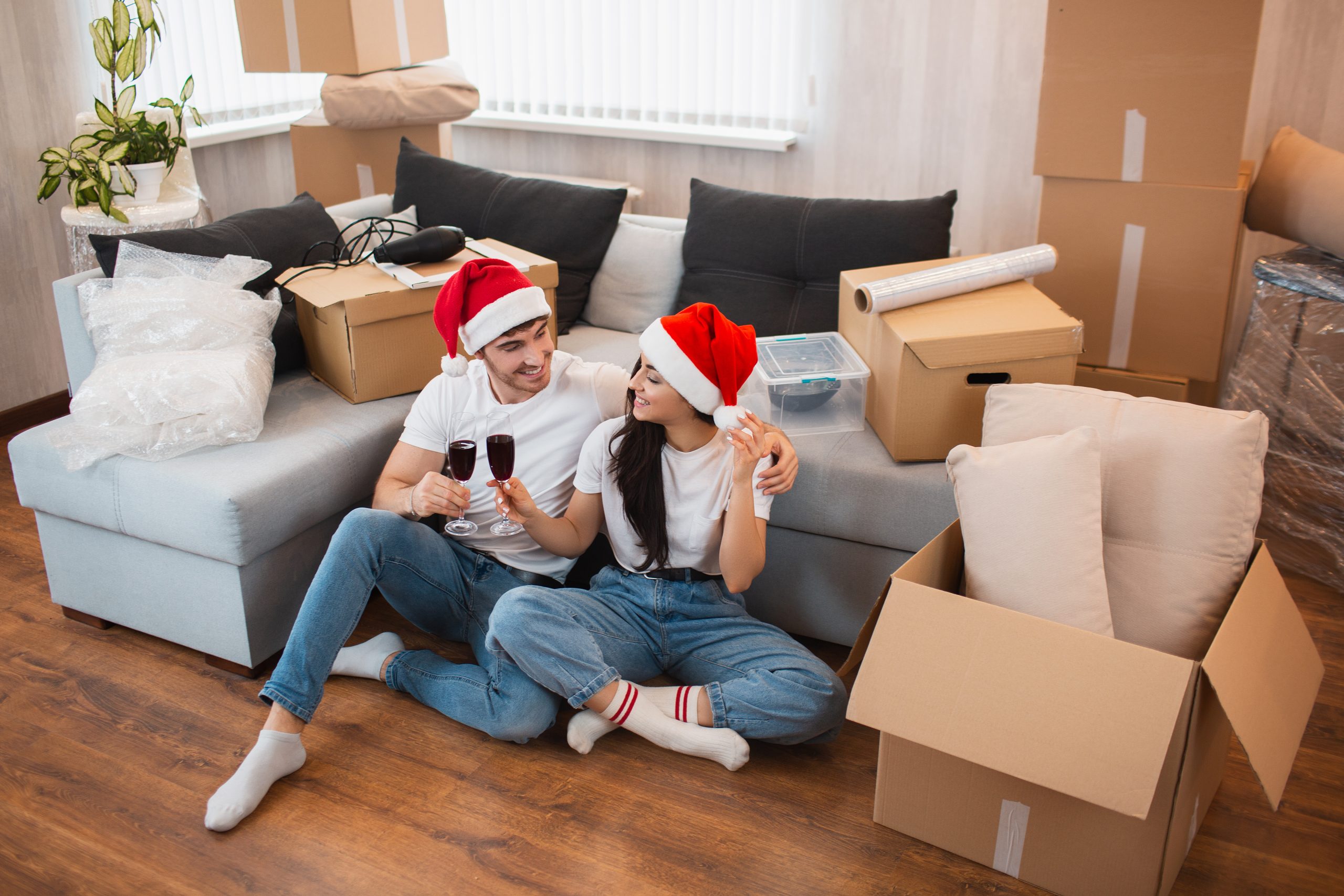 Newlywed couple celebrate Christmas or New Year in their new apartment. Young happy man and woman drinking wine, celebrating first christmas