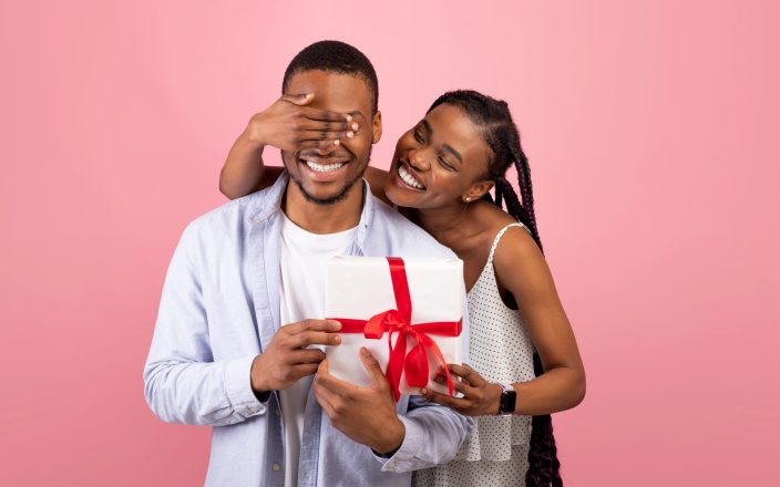 woman surprising boyfriend with gift covering eyes