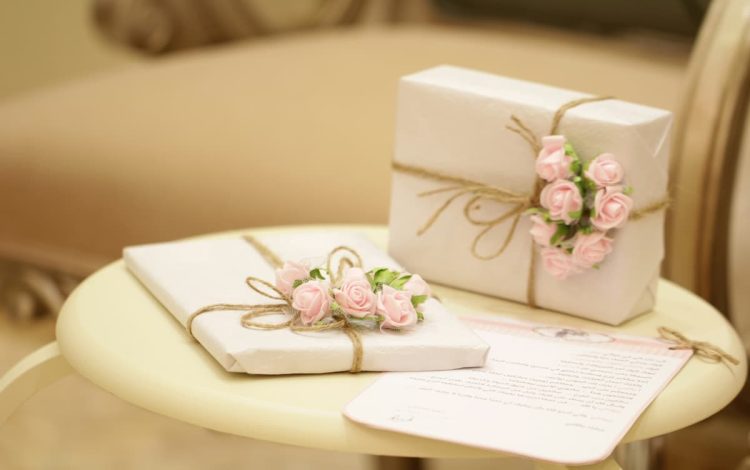 Beautifully wrapped wedding gifts with delicate pink floral decorations on a beige table, exemplifying modern wedding registry etiquette and personalized gift selections. Perfect representation for topics on wedding registry etiquette, wedding etiquette, and wedding registry tips for 2024.