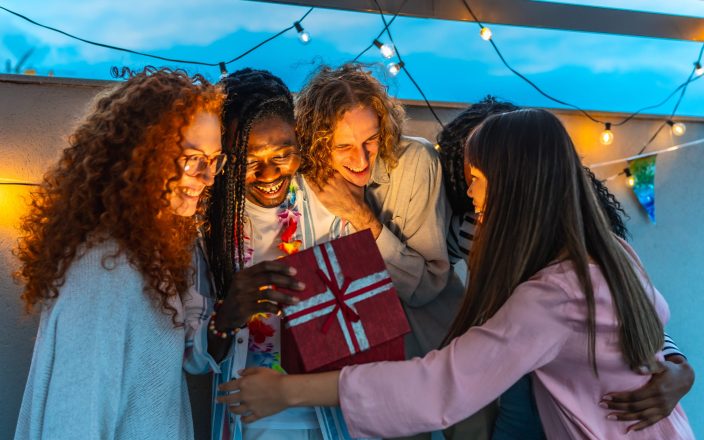 man opening birthday present embraced by his friends