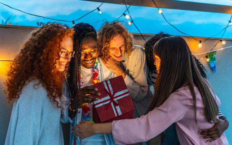 man opening birthday present embraced by his friends