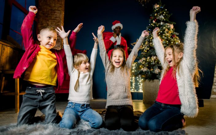 Beautiful young happy children raise their hands up, because African Santa Claus came and puts presents at the Christmas tree