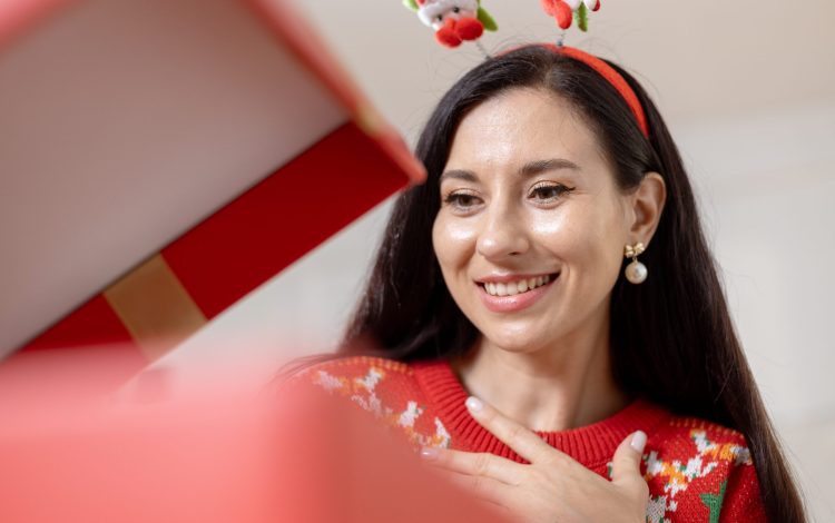 Christmas day concept. woman sitting surprised and opening gift box with christmas tree background. Festive atmosphere party.