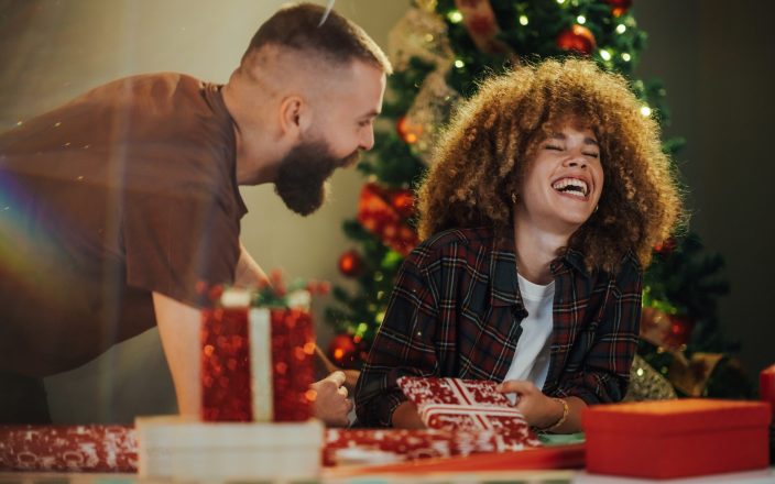 Couple happily wraps christmas presents together at a cozy table. Surrounded by festive decorations and twinkling lights. Sharing laughter and love as they prepare surprises for family and friends