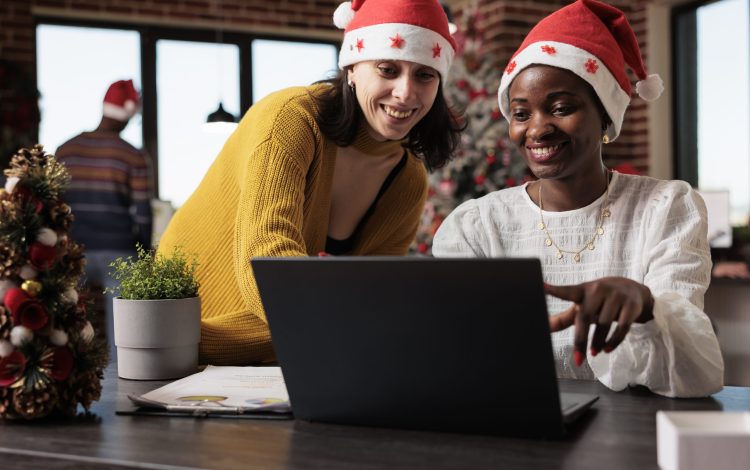 Coworkers doing teamwork in festive company office, working on laptop to plan project in space filled with christmas ornaments and lights. People at office job with xmas tree and decorations.