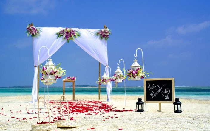 Beach destination wedding setup with a beautiful floral arch, lanterns, and a 'Just Married' sign. Ideal wedding registry gifts for a destination wedding include travel-friendly items and cash funds.