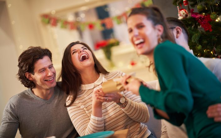 Picture showing group of friends pulling Christmas crackers at home