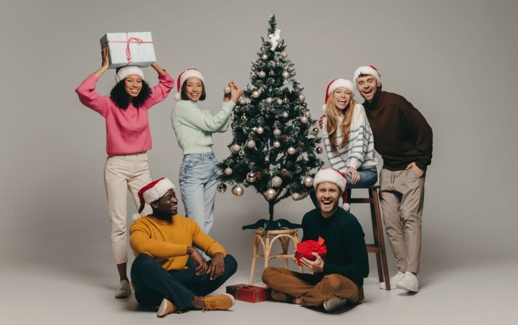 Group of young people smiling while having fun near the Christmas tree on studio background together