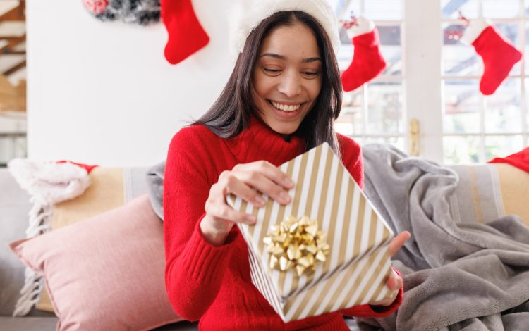 Happy biracial woman wearing santa hat, sitting on sofa in living room, having video call. Spending quality time at home alone at christmas.