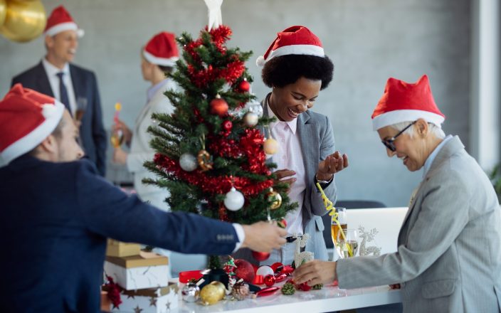 Happy African American businesswoman and her coworkers having fun while decorating Christmas tree in the office.