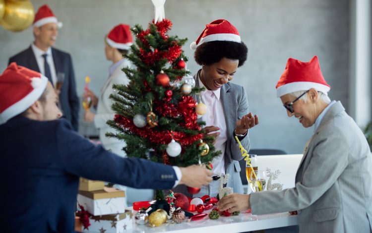 Happy African American businesswoman and her coworkers having fun while decorating Christmas tree in the office.