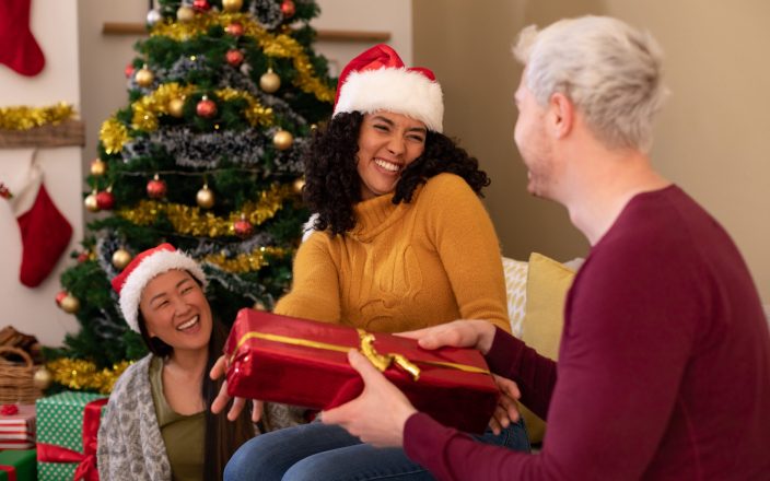 Happy diverse female and male friends sharing presents at christmas time. christmas festivities, celebrating at home with friends.