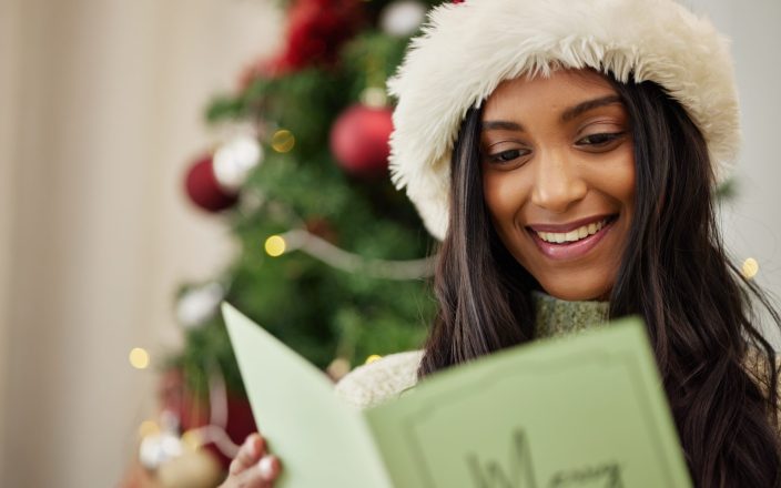 Happy woman reading Christmas card, note or message in home living room in winter holiday celebrati.