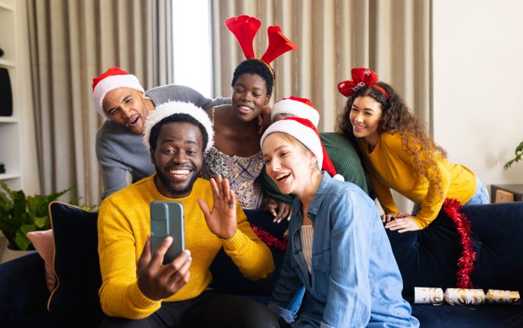 Image of happy diverse friends celebrating christmas at home making smartphone video call. Christmas, celebration, tradition, friendship, inclusivity and lifestyle concept.