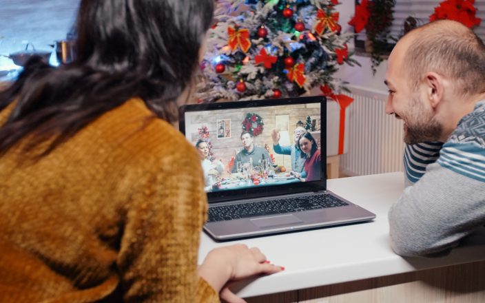 Man and woman using video call communication talking to family on christmas eve. Couple chatting with relatives on online remote conference, celebrating holiday festivity in decorated kitchen.