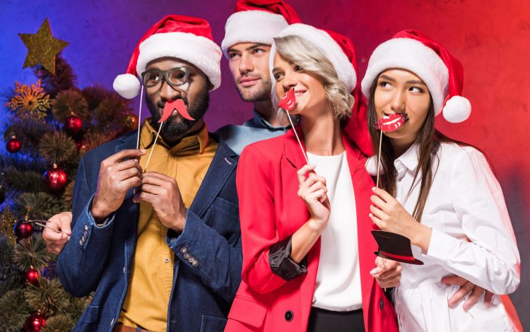 multicultural businesspeople holding lips and glasses on sticks at Christmas corporate party