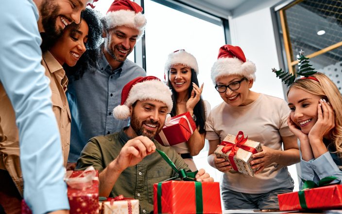 Secret Santa. A smiling man unpacks a Christmas present from colleagues at work. New Year's eve.