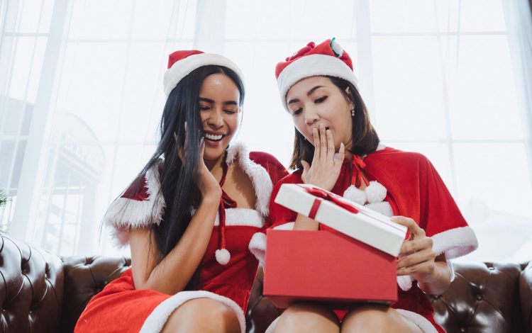 Two Santa women open gift boxes together.