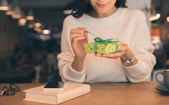 Woman opening gift over desk with book and phone next to her