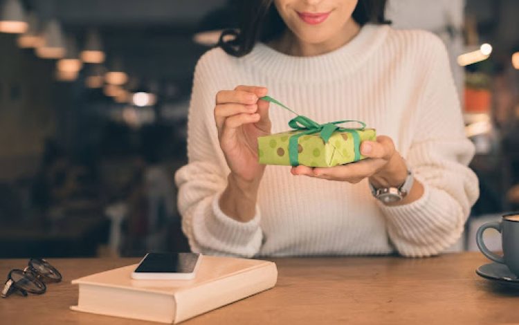 Woman opening gift over desk with book and phone next to her