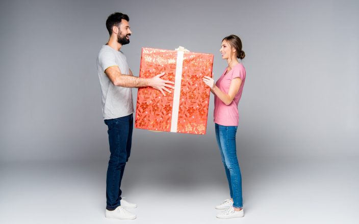 Young couple standing with big red gift box isolated on grey