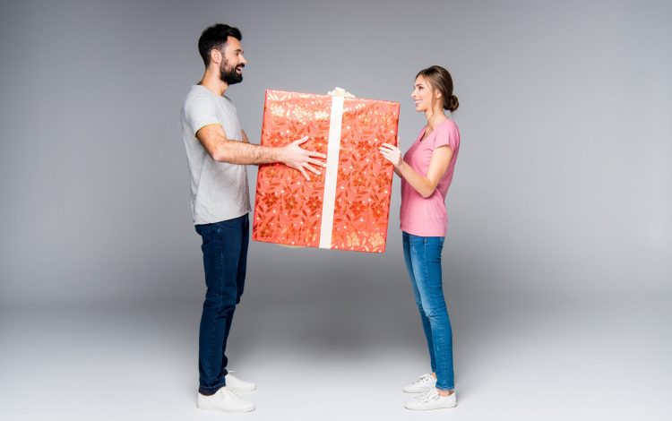 Young couple standing with big red gift box isolated on grey